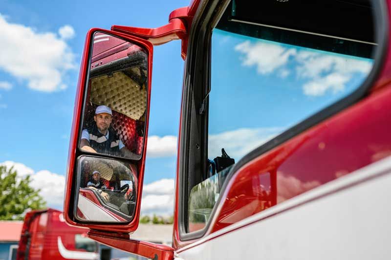 View of a truck driver from the seat of his rig in the rearview mirror.